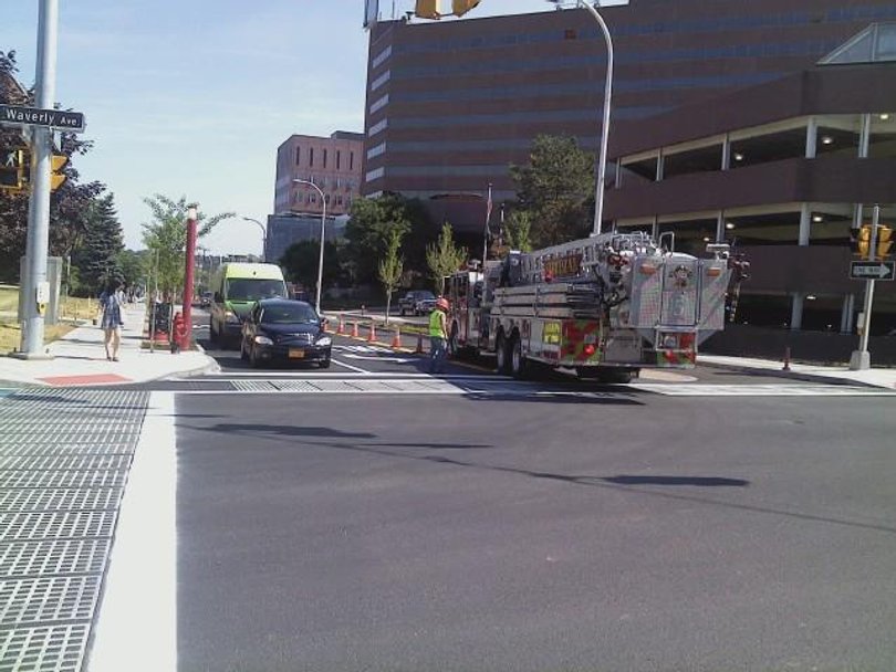 Cars and a firetruck travel both ways down the street. The firemen in the firetruck stopped and asked a construction worker if they could turn down University Avenue. He told them they could.

