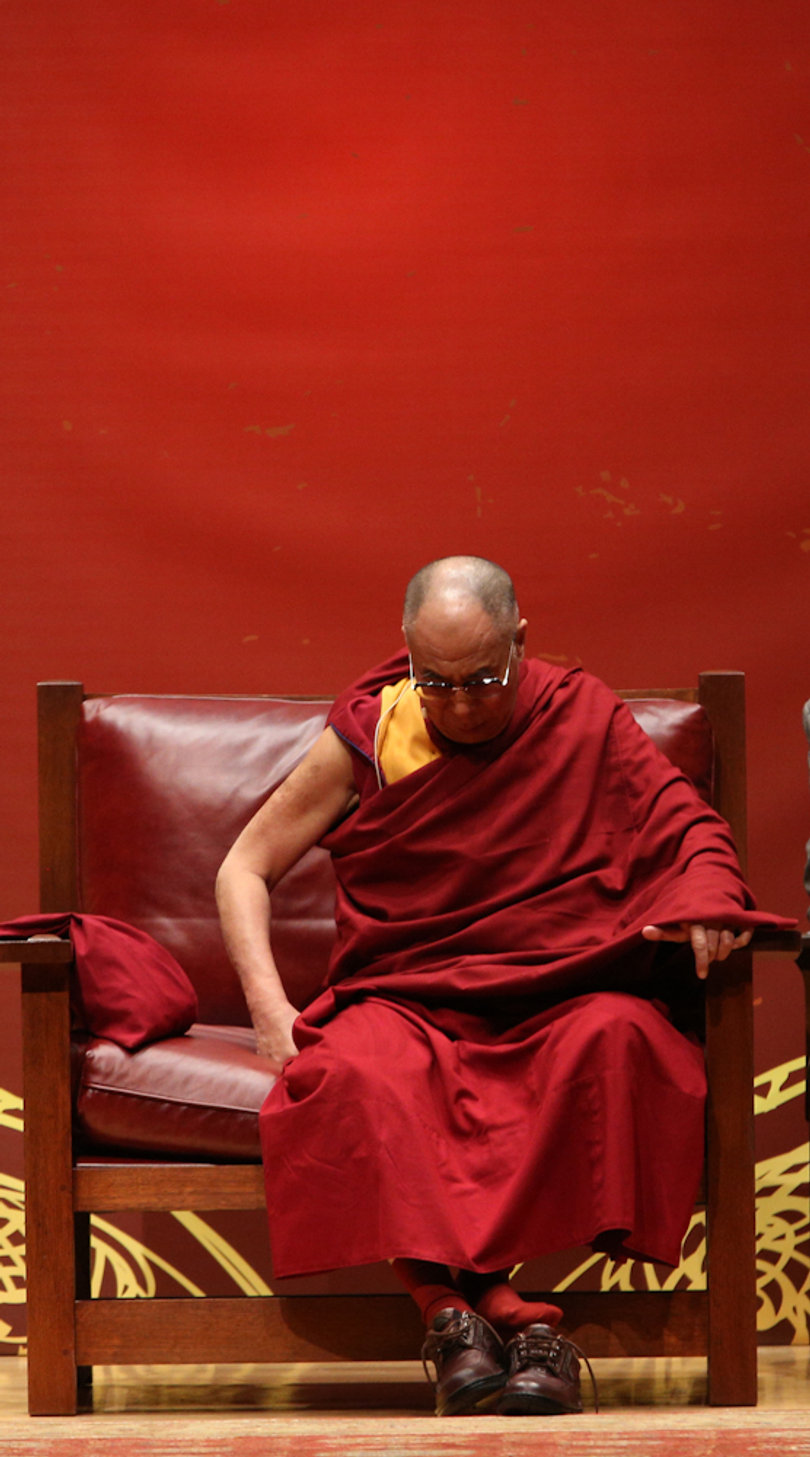 The Dalai Lama takes off his shoes at Monday's morning panel. 