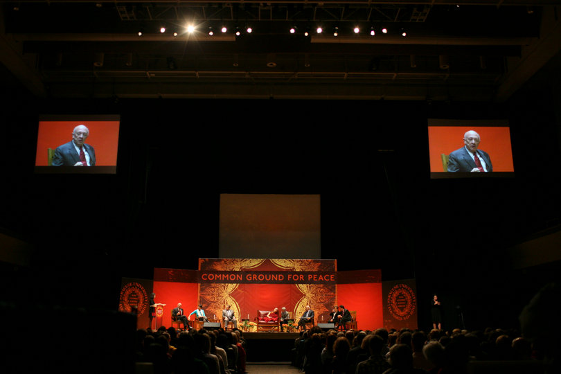 A wide look at the stage set in Goldstein Auditorium for the "Common Ground for Peace" panels Monday. On the video screens, R. James Woolsey, former head of the CIA, participates in the discussion.