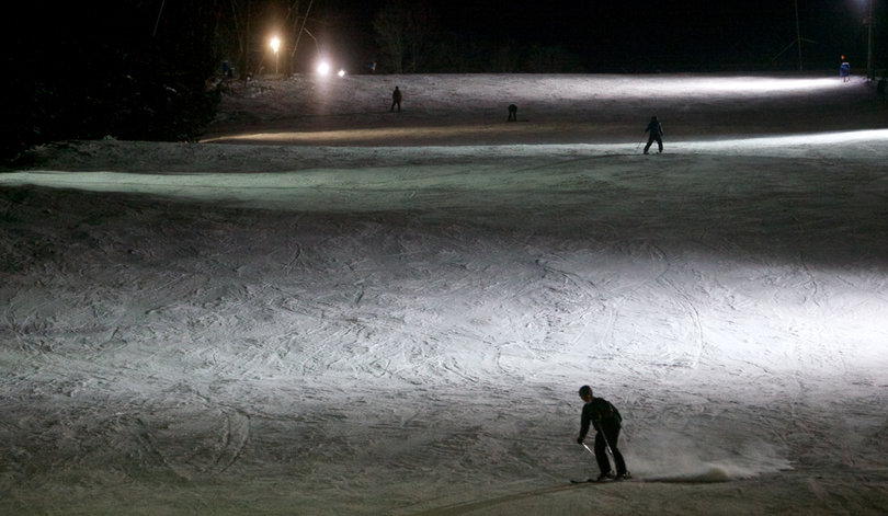 The nighttime skiers and snowboarders trek downhill on Toggenburg Mountain.