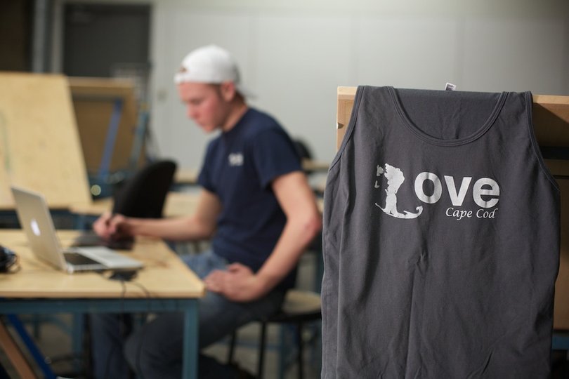 Tyler Poyant sits and works at his studio in the Shaffer Art Building. Poyant created the design for his line of shirts based on the shape of the Cape Cod peninsula.