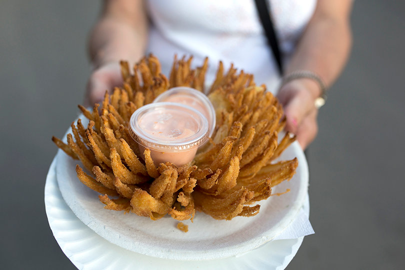 A visitor shows off a blooming onion, which is an onion that has been deep fried to a golden brown. Fried food vendors boast turning anything and everything into a fried delicacy.