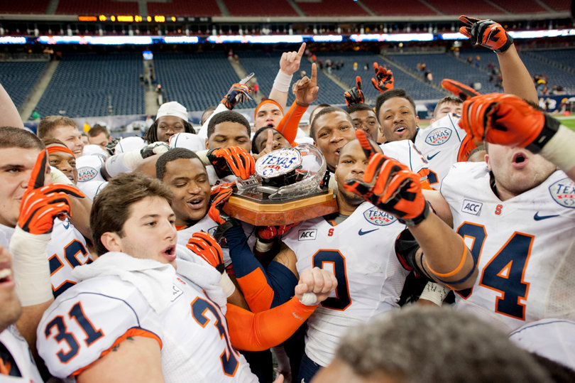 As one, Syracuse lifts the Texas Bowl trophy at midfield.