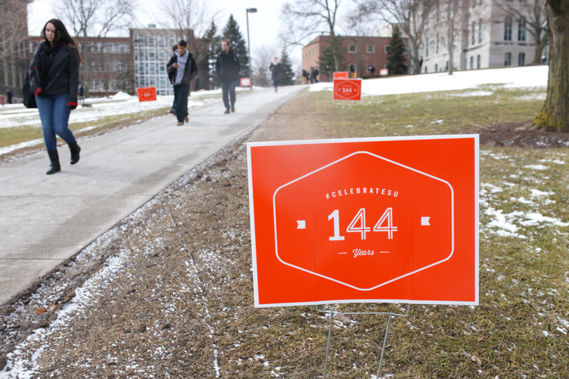Students walk past 144th SU birthday signs in front of the Hall of Languages. Signs were posted all over campus by the Office of Alumni Relations.                          