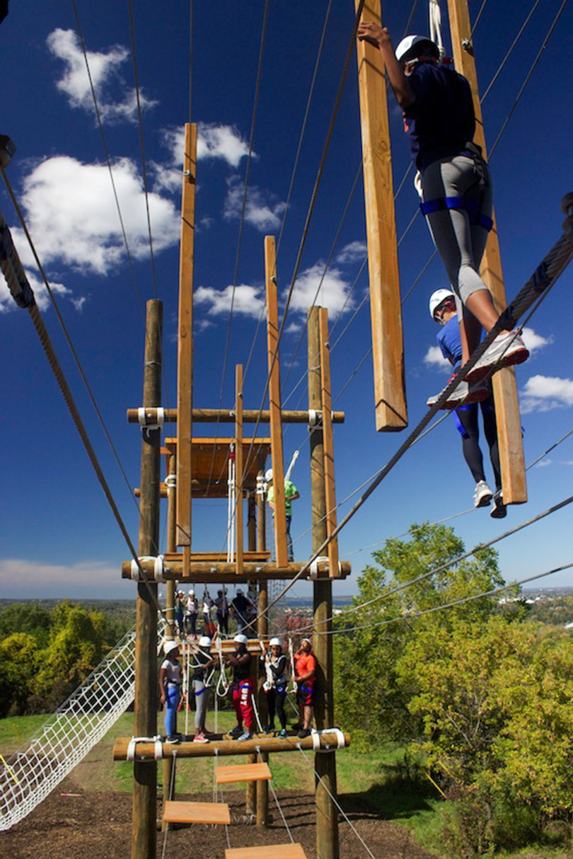 A group climbs across the ropes at the outdoor challenge course. 