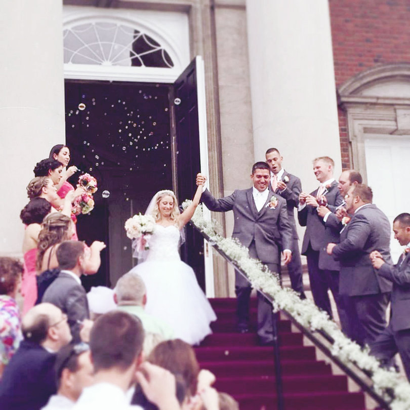 Melissa and Joe Rocco walk down the chapel steps, cheered on by their family and friends. The two met in Boston at their first day of work.