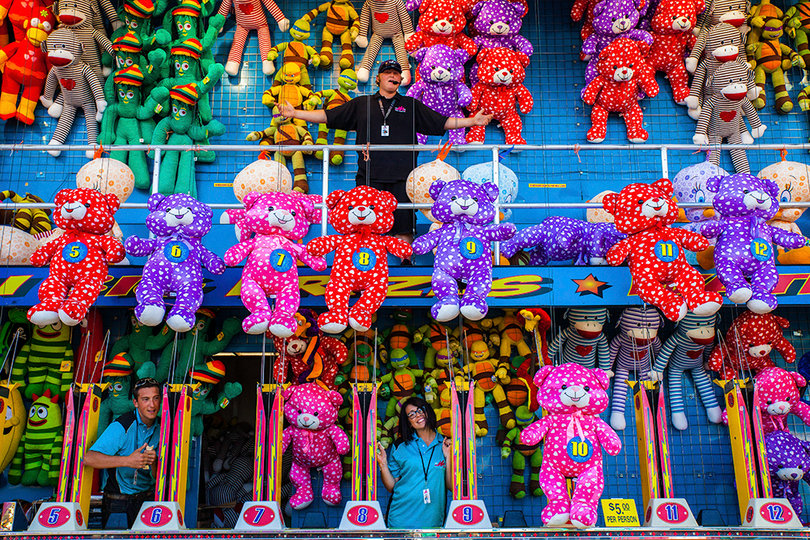 Energetic hosts of a game booth at The Great New York State fair encourage visitors to join a water gun competition to win one of the colorful plush prizes at the New York state fair. Winners could choose from teddy bears, sock monkeys and more.