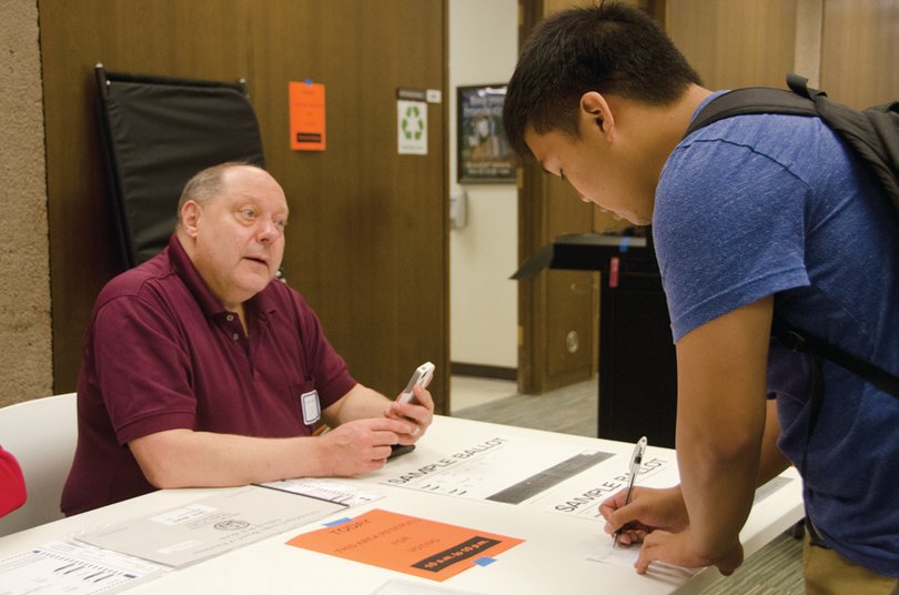 Timothy Liebe (left) and Benjamin Fang (right) talk at a sign-in table at Bird Library before Fang voted in Tuesday’s primaries.