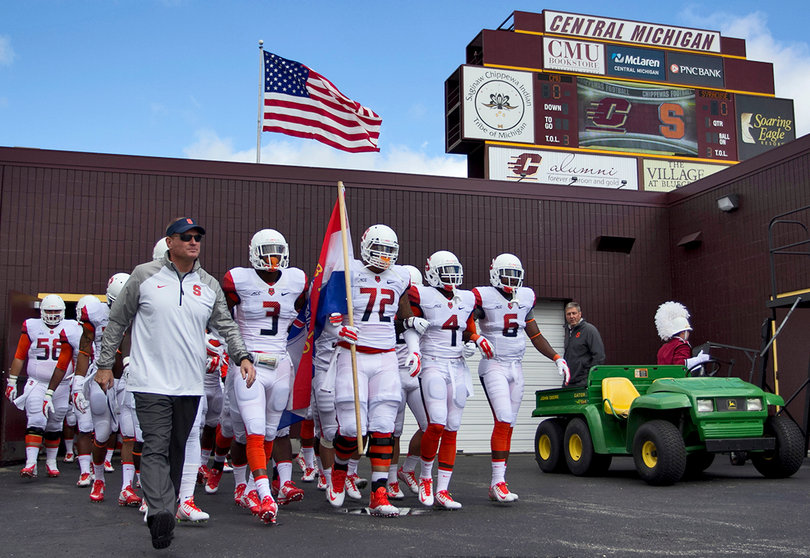 Head coach Scott Shafer leads his team onto the field as offensive lineman Ivan Foy (72) carries a flag.