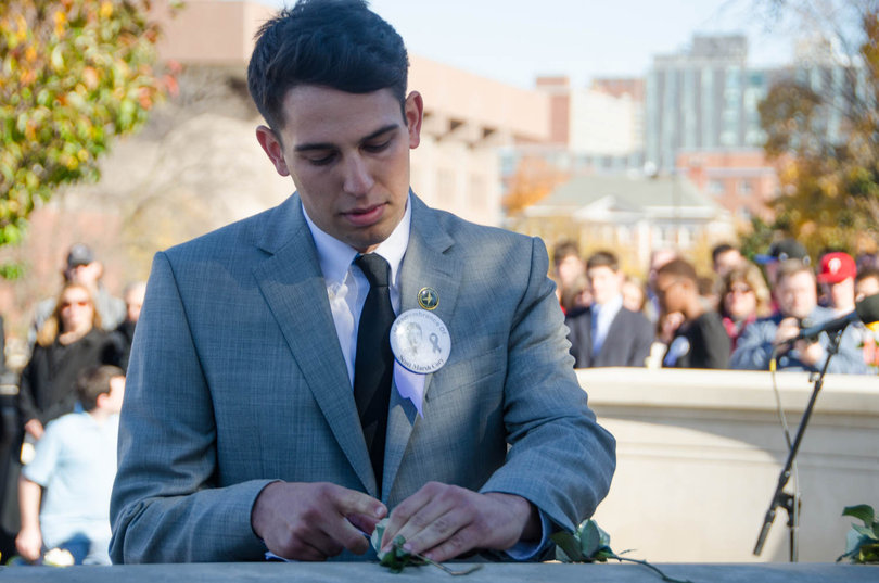 Bo Stewart, a senior with majors in economics, policy studies, political science, spanish language and literature and culture and a Remembrance Scholar, places a rose on the wall to commemorate Scott Marsh Cory, a Pan Am Flight 103 victim. 