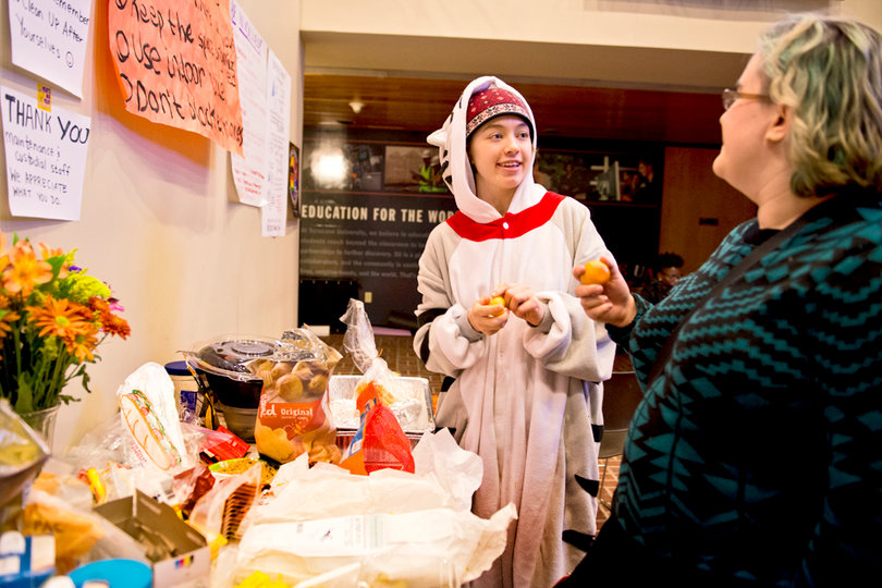 Jules Struble and Madeleine Slade talk near THE General Body’s food table and protest signs in Crouse-Hinds hall. 