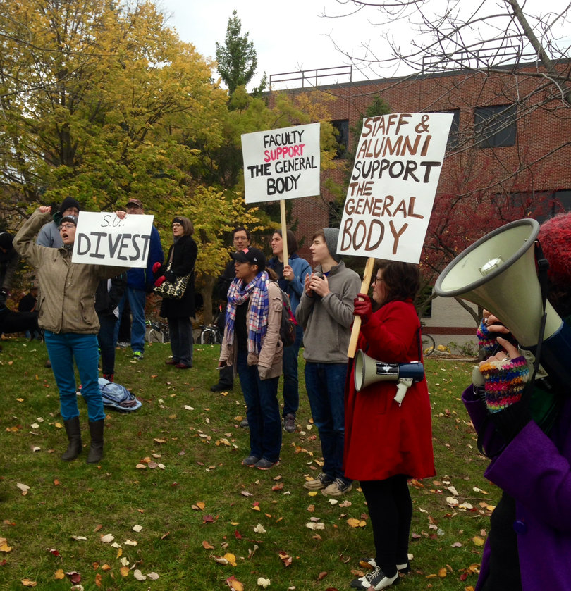 Protesters stand in front of Crouse-Hinds Hall holding signs to show their support for students staging a sit-in inside.
