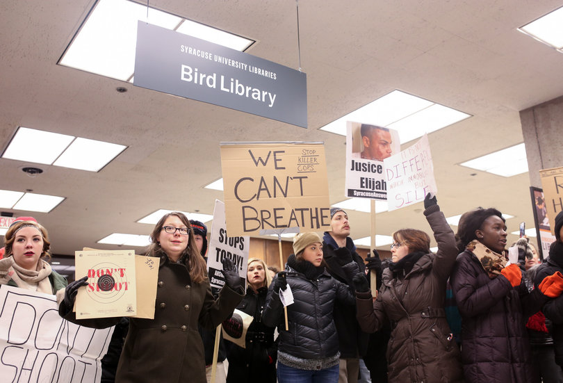 Protesters hold up signs upon their arrival to Bird Library, where they held a "die-in" on Monday afternoon.
