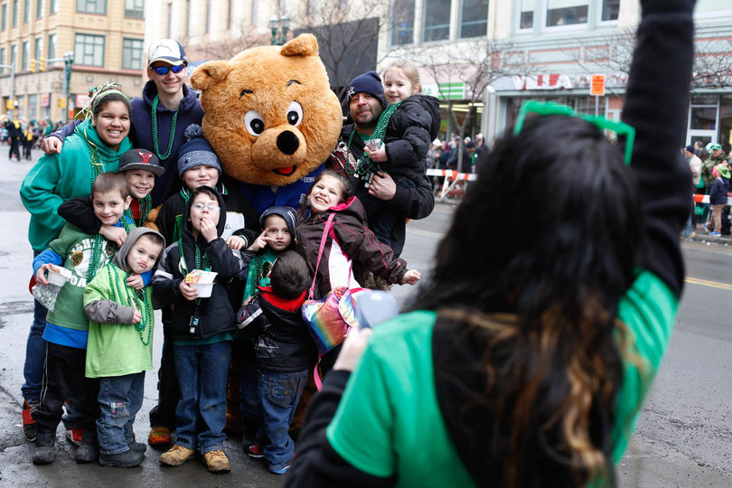 Families at the Syracuse St. Patrick's Day Parade on Saturday pose with a bear mascot for a local pharmacy that accompanied the float.
