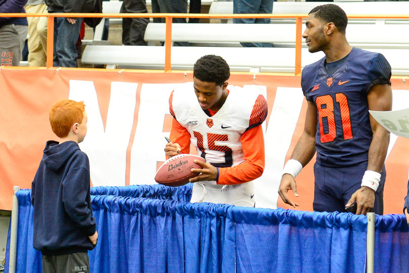 Syracuse cornerback Juwan Dowels, standing next to wide receiver Jamal Custis, signs an autograph for a young fan after SU's spring game.