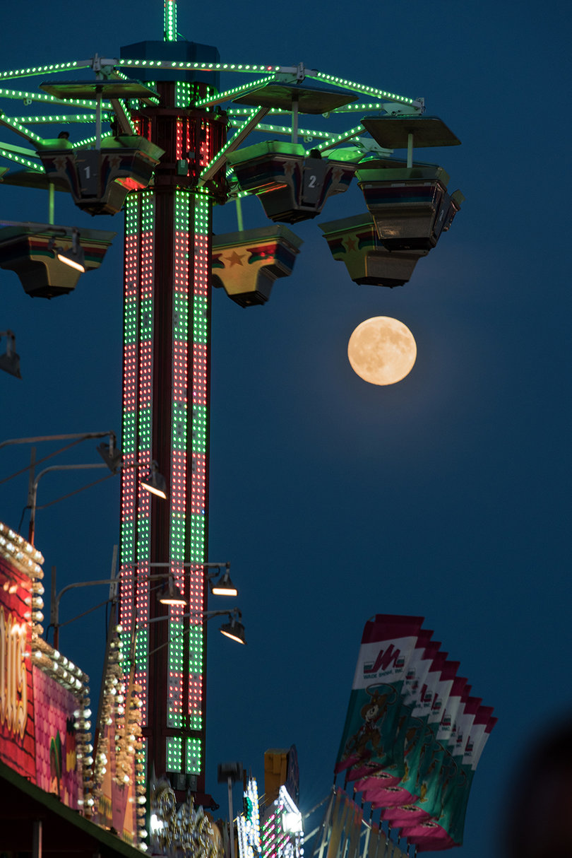 The moon shines brightly as the ride's lights illuminate the night. 