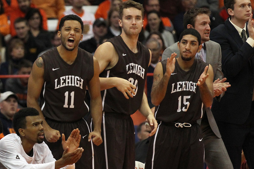 A trio of Lehigh players stand on the sideline rooting on their fellow Mountain Hawk players on the court.