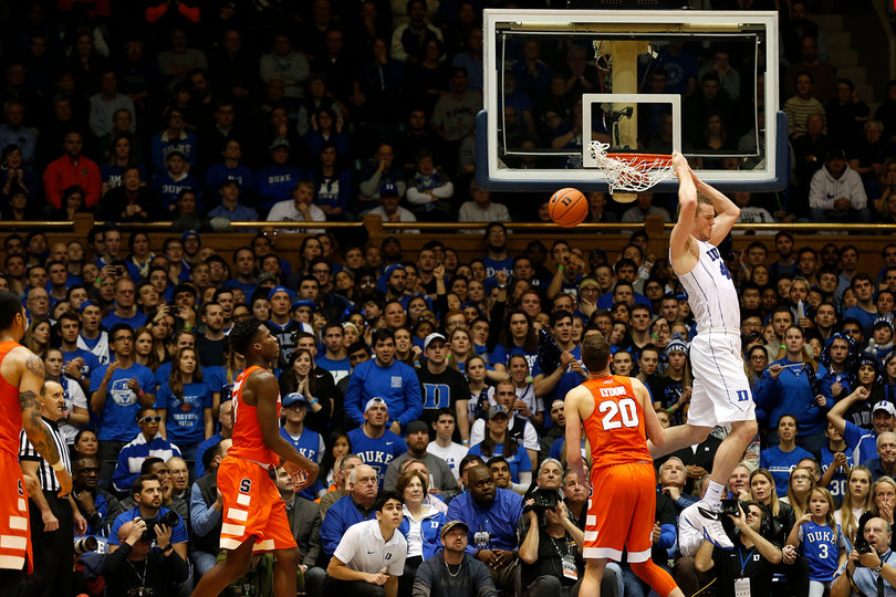 A Duke player hangs on the rim after throwing down a slam dunk and Lydon watches from underneath the basket.
