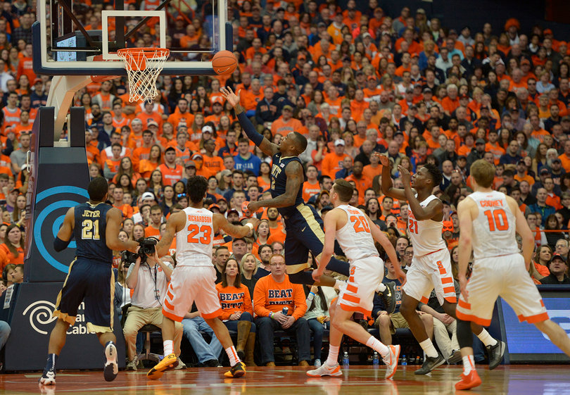 A Pittsburgh player attempts a layup with his right hand with four nearby Syracuse players simply watching him go up uncontested.