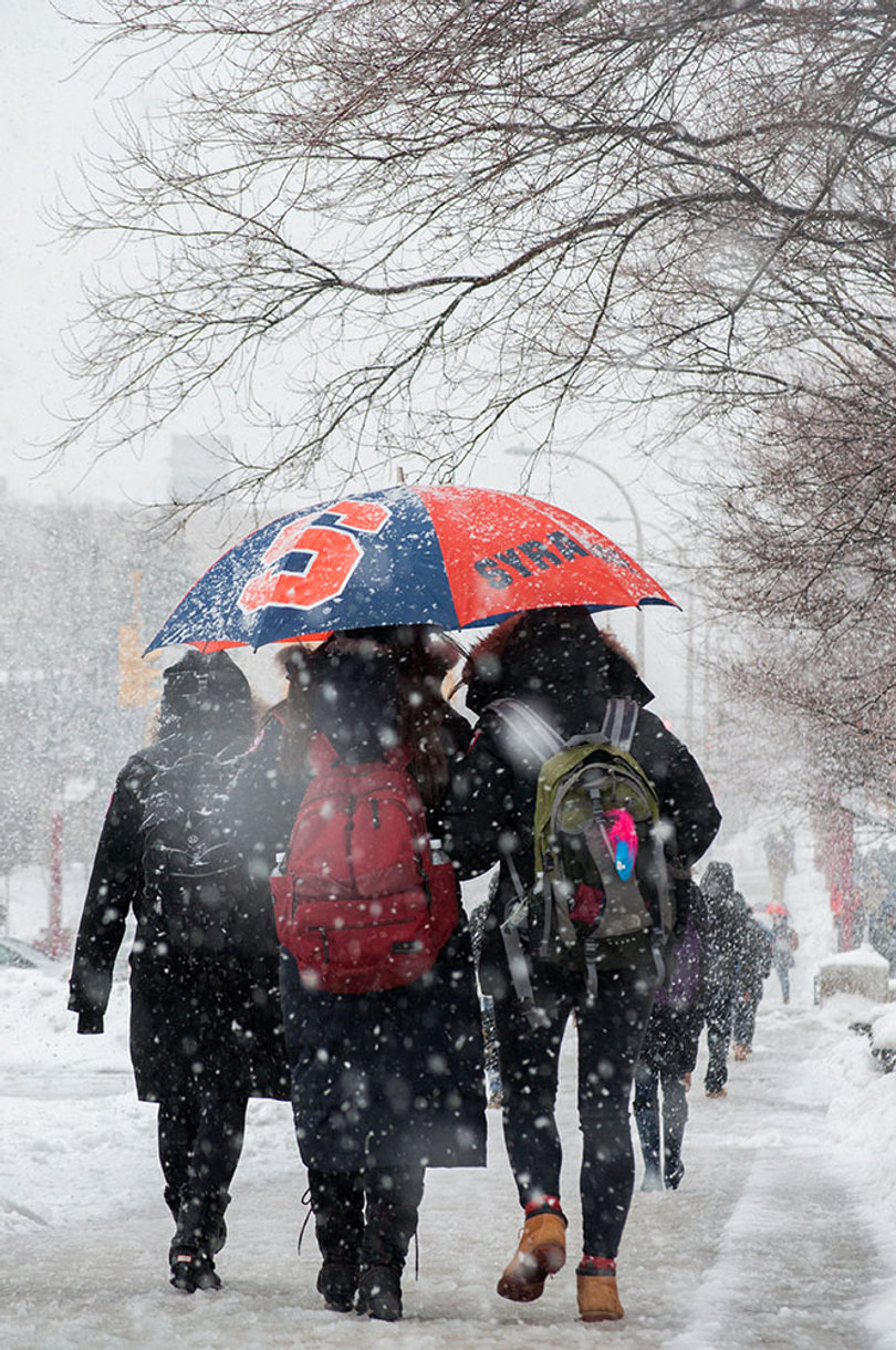 Students walk on a sidewalk  on Syracuse University's campus as snow falls.
