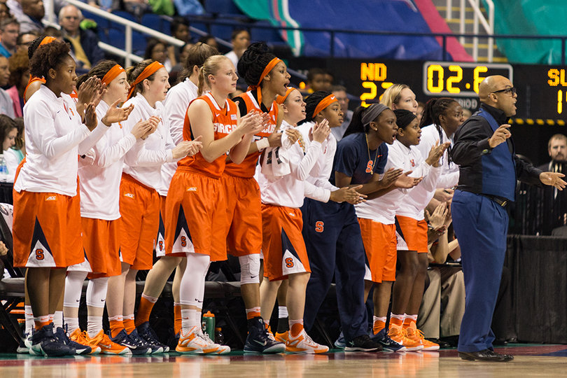 The Syracuse bench stands in support of their team, lead by head coach Quentin Hillsman in the navy suit on the far right.