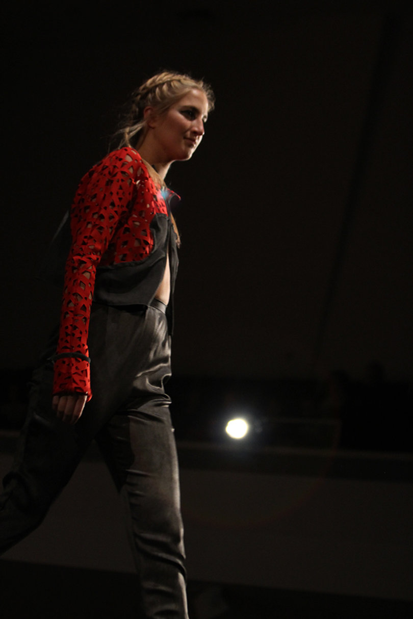 A model marches onto the stage in a red and black cutout ensemble by Nicole Brown.