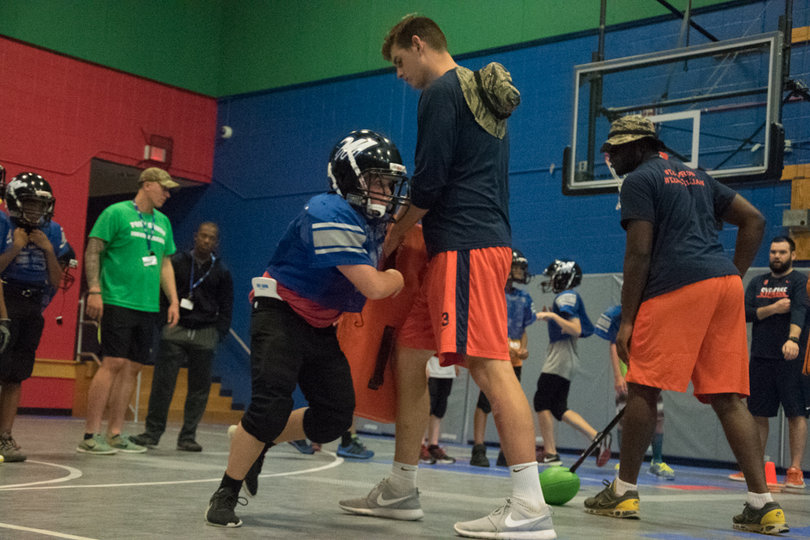 Junior long snapper Nathan Hines holds a pad as a youth player runs by.