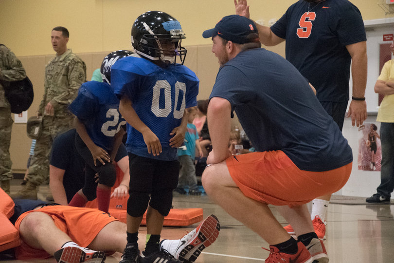Former Syracuse lineman Macky MacPherson squats as he speaks with a player at the clinic.