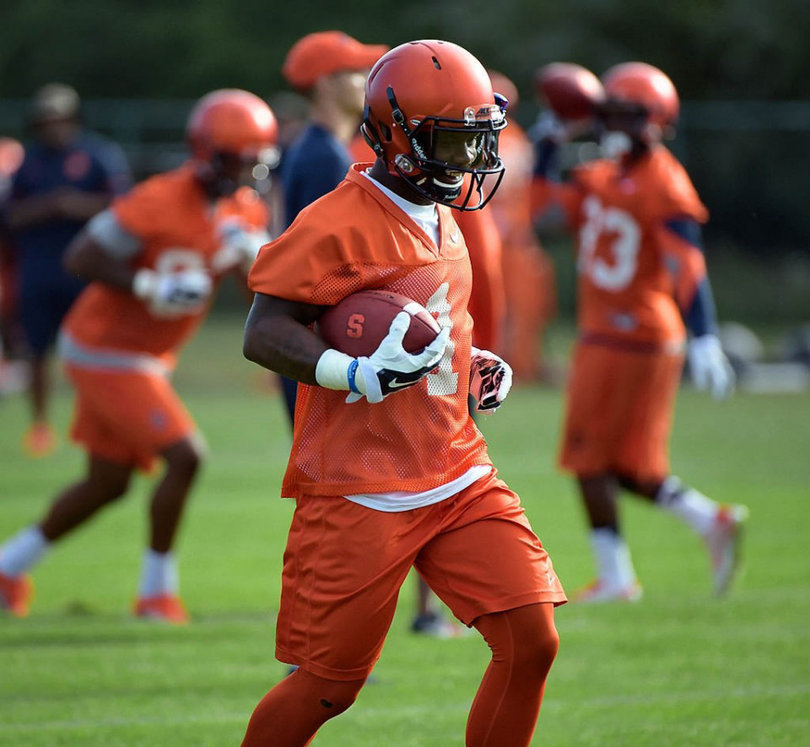 Wide receiver Brisly Estime carries the ball in his right hand with a smile on his face.