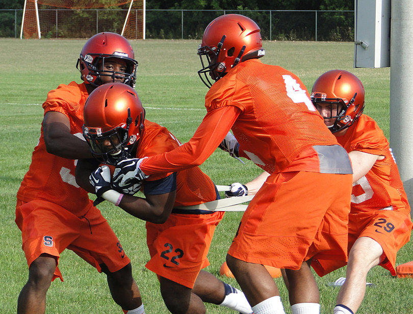 Jordan Fredericks (22) performs a drill as other members of the running backs unit try to hold him back or reach for the ball.