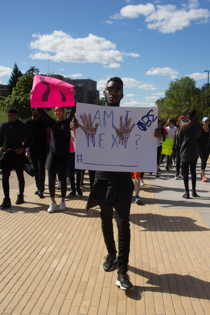 Dominic Samuels, president of the Syracuse University chapter of the Phi Beta Sigma fraternity, holds an "Am I Next" sign with a hashtag at the bottom and an open space next to it for the next name of a victim of police brutality.