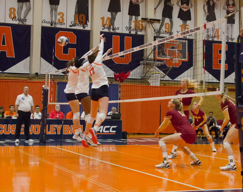 Three Syracuse players hold their hands up above the net as the ball flies past them.