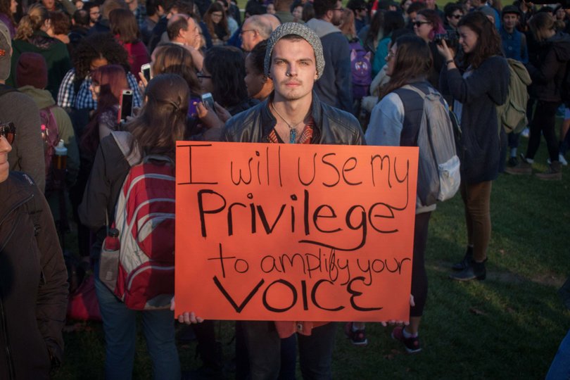 Daniel Roezter, a senior international relations major at Syracuse University, holds a sign reading "I will use my privilege to amplify your voice."