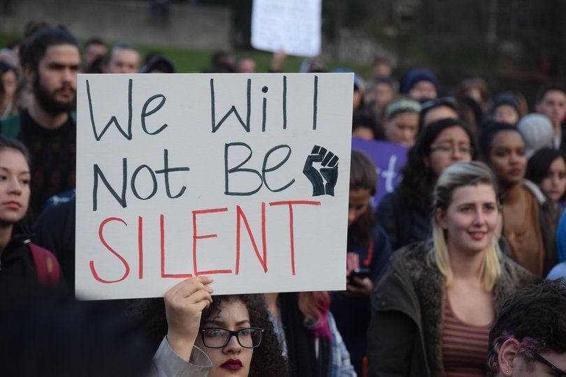 A student holds a sign that reads "we will not be silent."