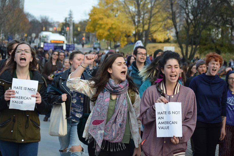 Students chant while holding papers that say "hate is not an American value."