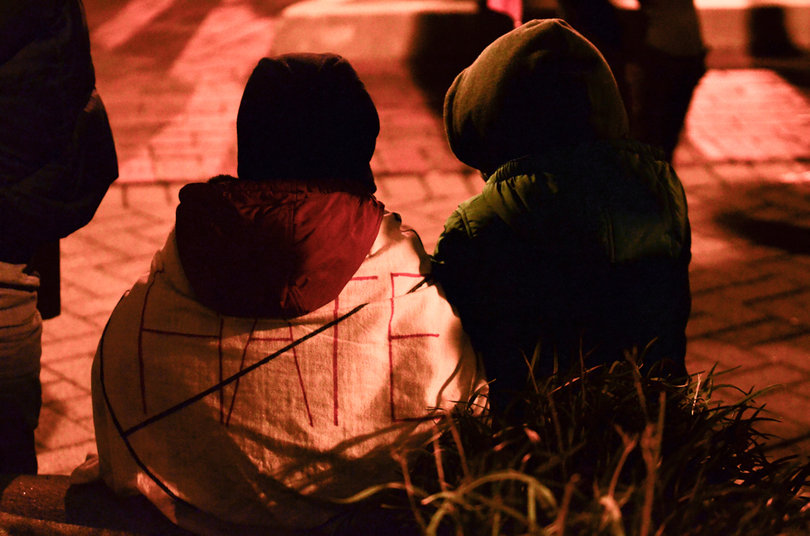 Two Syracuse residents sit during the protest. One wears blanket with the word "hate" crossed out. 