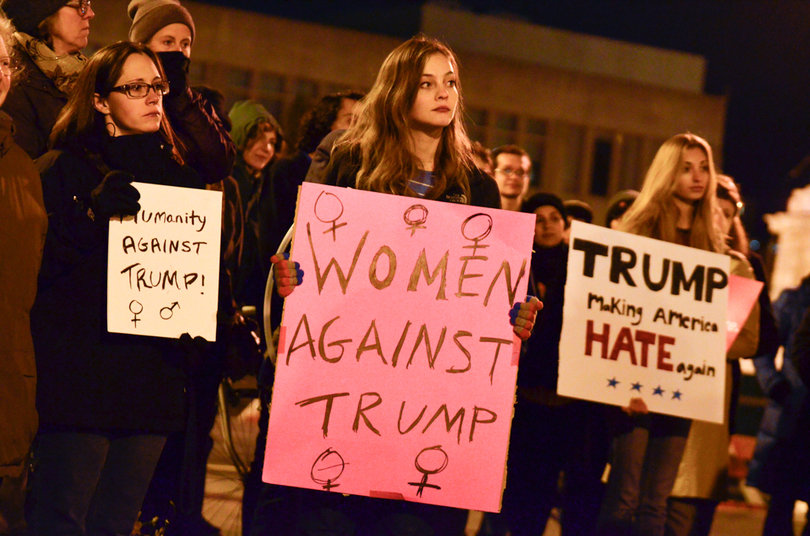 Women hold signs, protesting the election of Donald Trump. 