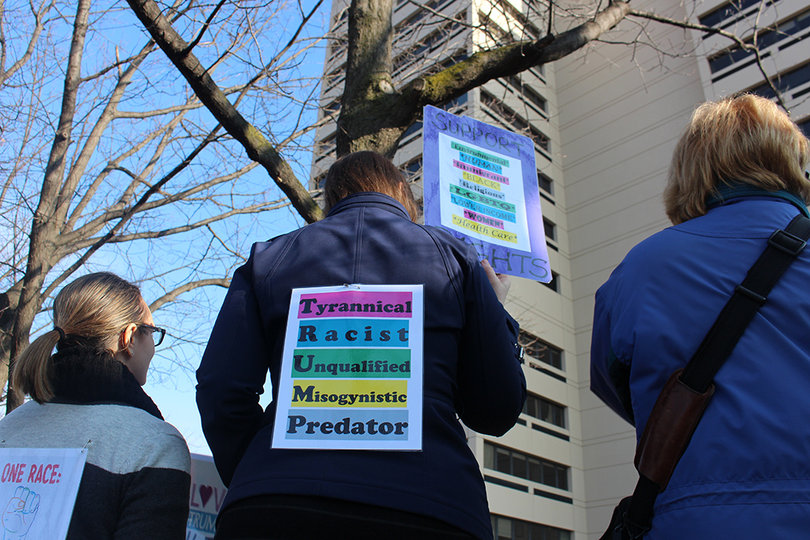 A woman wears an acrostic poem, calling Trump a "Tyrannical, racist, unqualified, misogynistic, predator." Acrostics using Trump's name have been popular during recent protests.