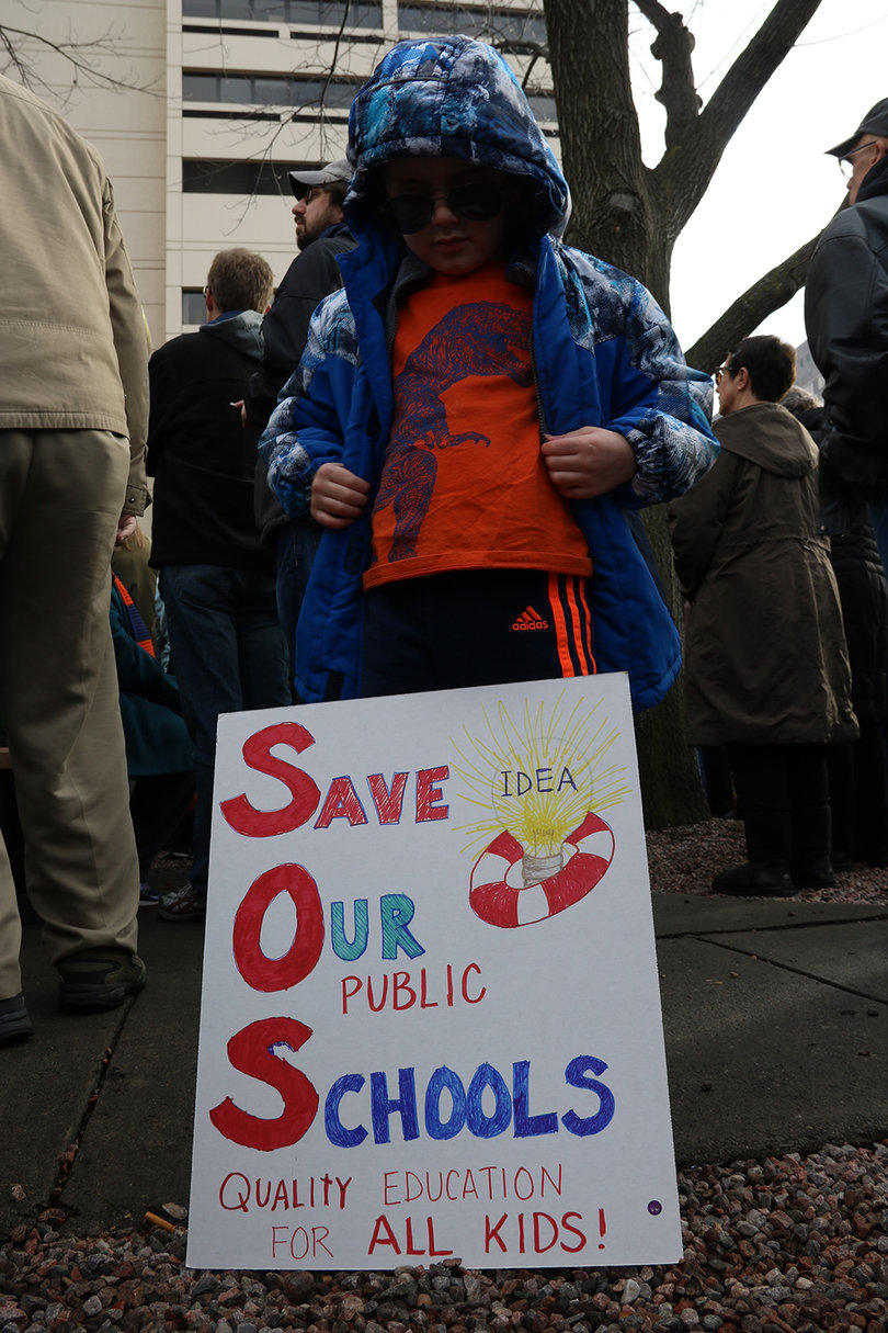 A child stands behind a sign that says "Save our schools." Education was another important theme of the march and the crowd booed at the mention of Betsy DeVos.
