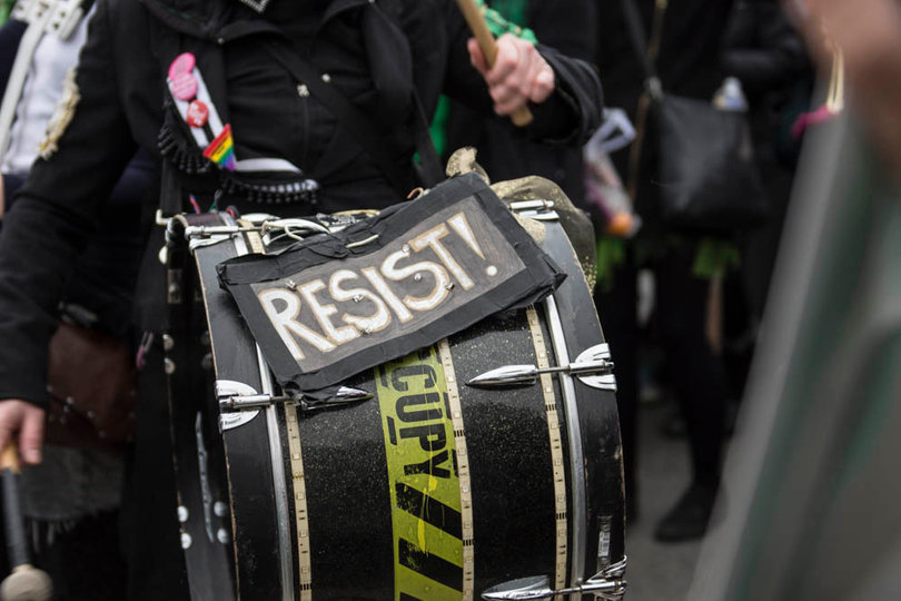 A group of musical performers with instruments play music and lead chants while women march towards the national monument. When asked where they were from, they answered "Everywhere."