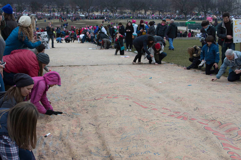 People sign their names and write messages on a scroll titled "We, The People" on a hill adjacent to the Washington Monument.