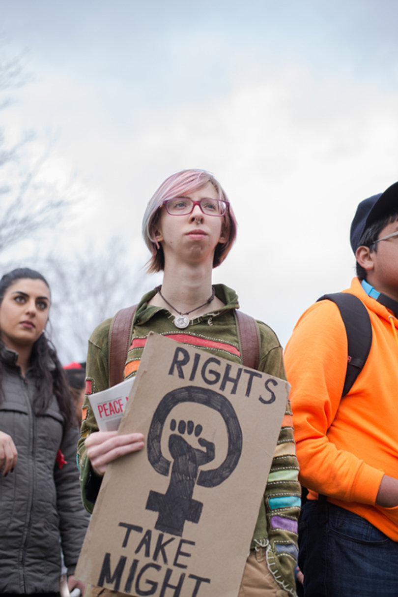 A community member holds a sign that reads "Rights Take Might" as they listen to a speaker.