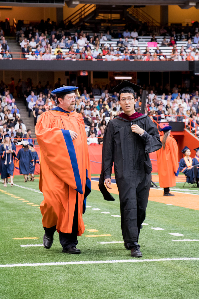 Syracuse University faculty members chat as they walk onto the field. 