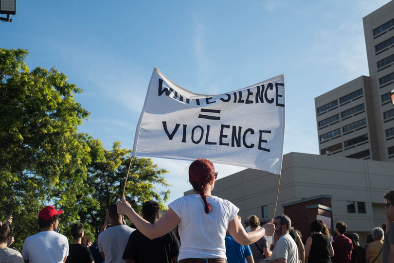 Nikeeta Slade holds a sign that says "White Silence = Violence" backwards so the people behind her could see it.