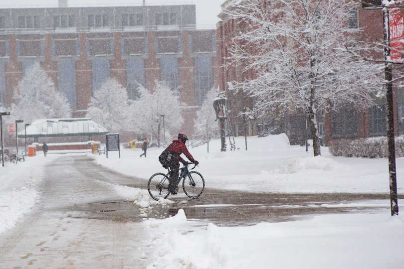 A man rides a bicycle near Syracuse University's College of Visual and Performing Arts on Friday during the snowstorm.