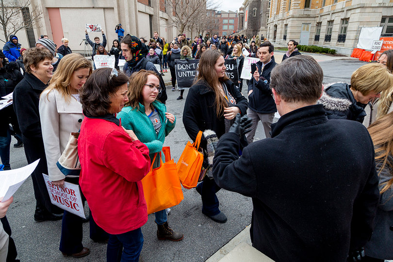 Admitted students and parents are greeted by university officials at a Carrier Dome entrance as student protesters scream chants and hand out flyers.