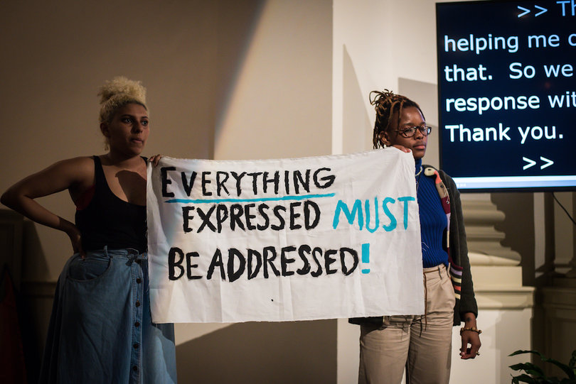 Two students hold a sign that reads, “EVERYTHING EXPRESSED MUST BE ADDRESSED.”
