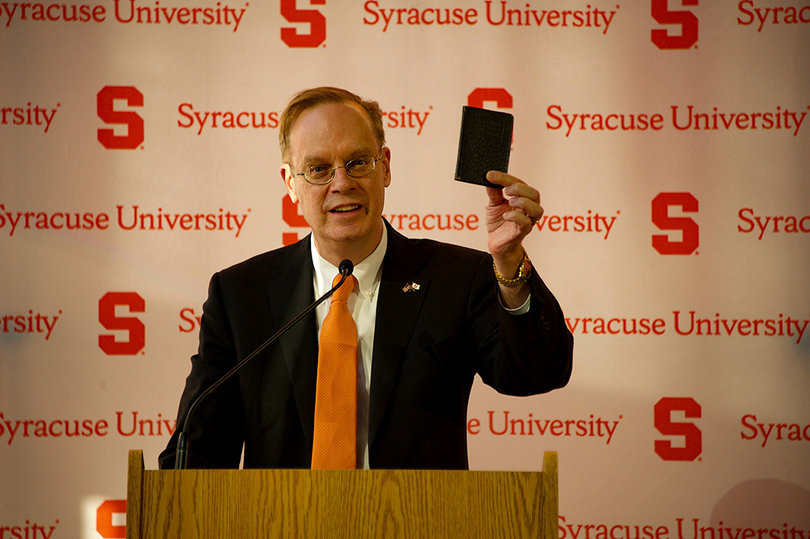 The chancellor holds up an SU rule book from 1923, which students were required to carry at all times. He said it shows "it really mattered to people to be Orange."
