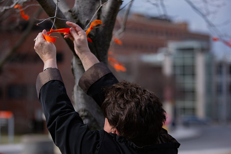 A person ties an orange ribbon to a tree outside of the S.I. Newhouse School of Communications.