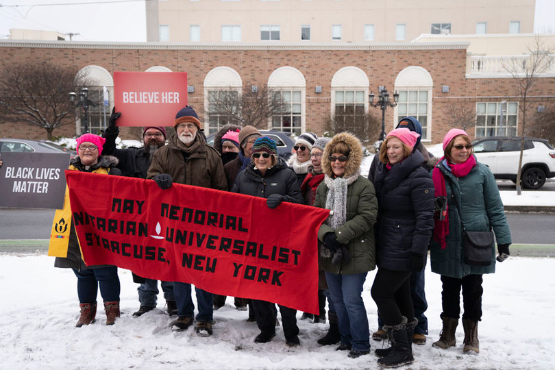 Protesters hold a banner of Syracuse's May Memorial Unitarian Universalist Society, one of several community groups that supported Saturday's march. 